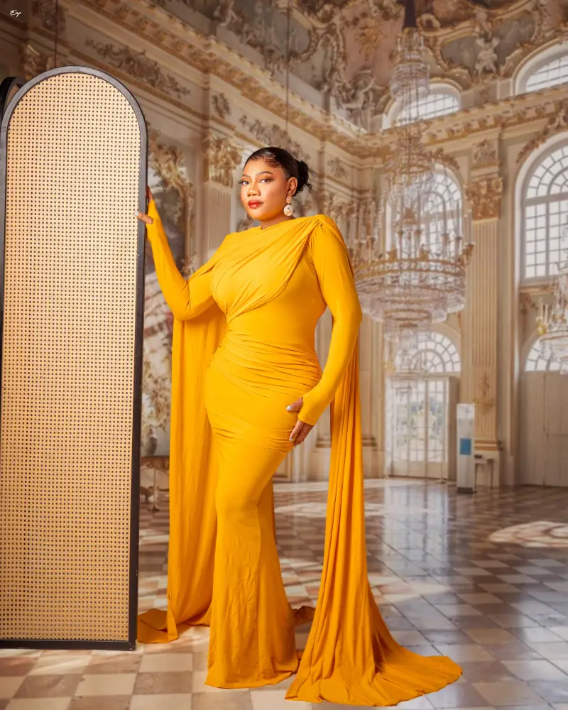 A marigold Ablizz column gown with a long draped cape, in a gilded hall